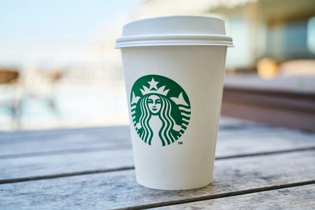 A disposable coffee cup with a lid outdoors on a wooden table, featuring a popular global logo.