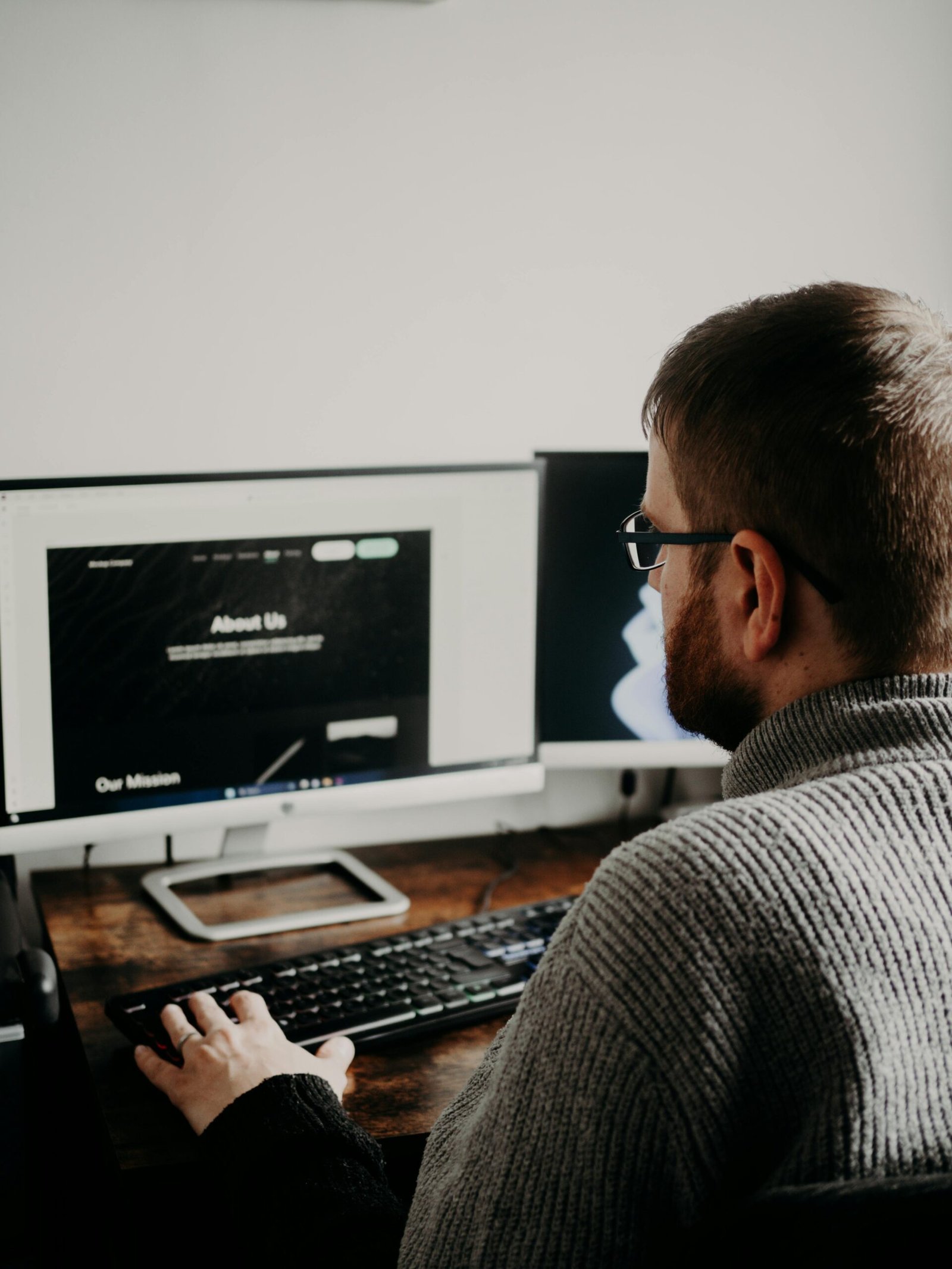 Man working on web design at home office setup with dual monitors.