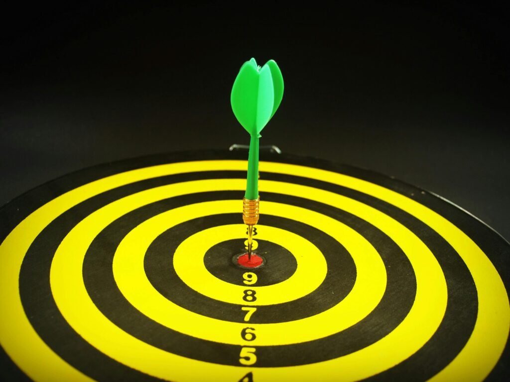 Close-up of a green dart hitting the bullseye on a yellow and black target board, symbolizing precision and success.